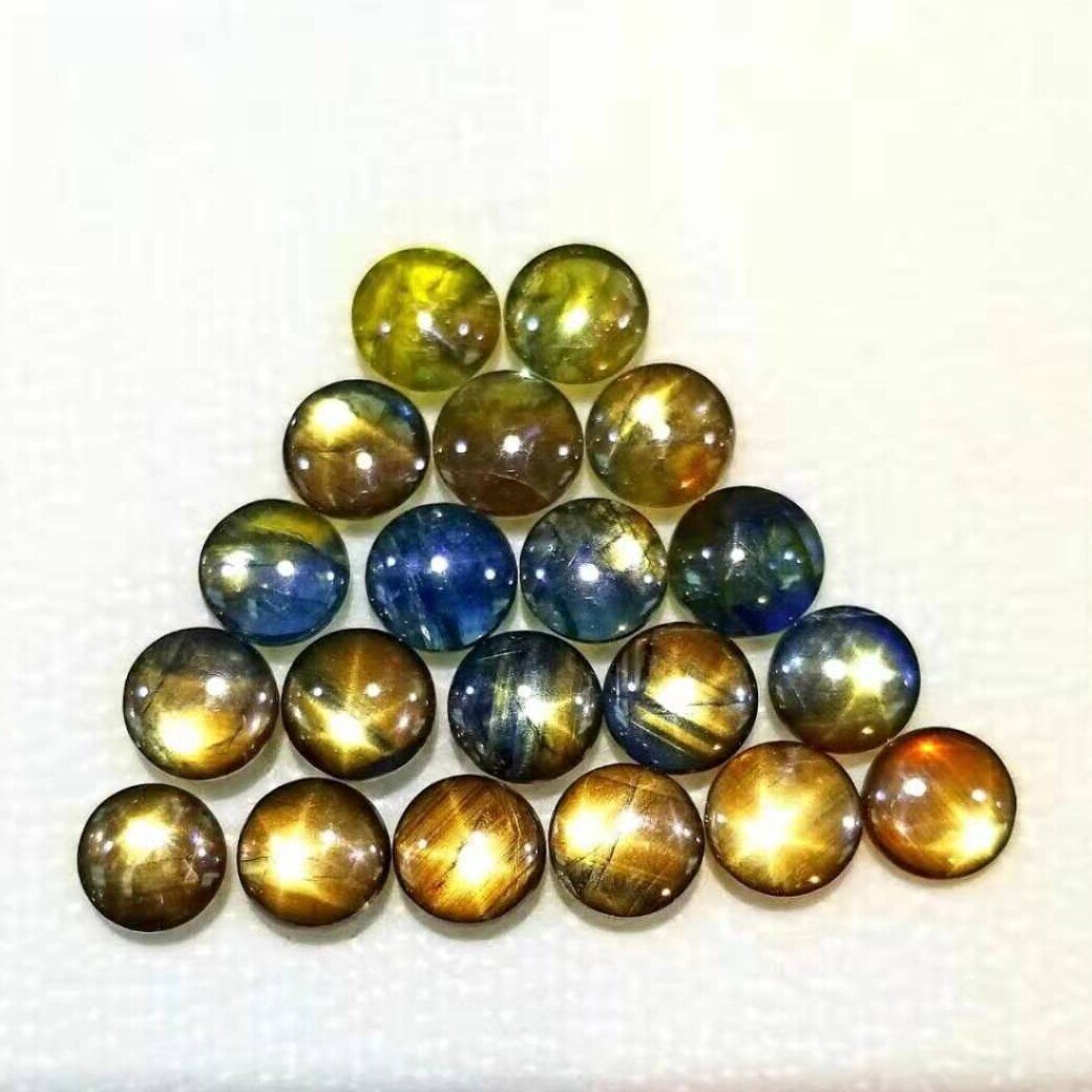 Twenty round gold sheen sapphire cabochons arranged in a triangle, in yellow, green, blue, gold and brown, several with six-rayed stars.