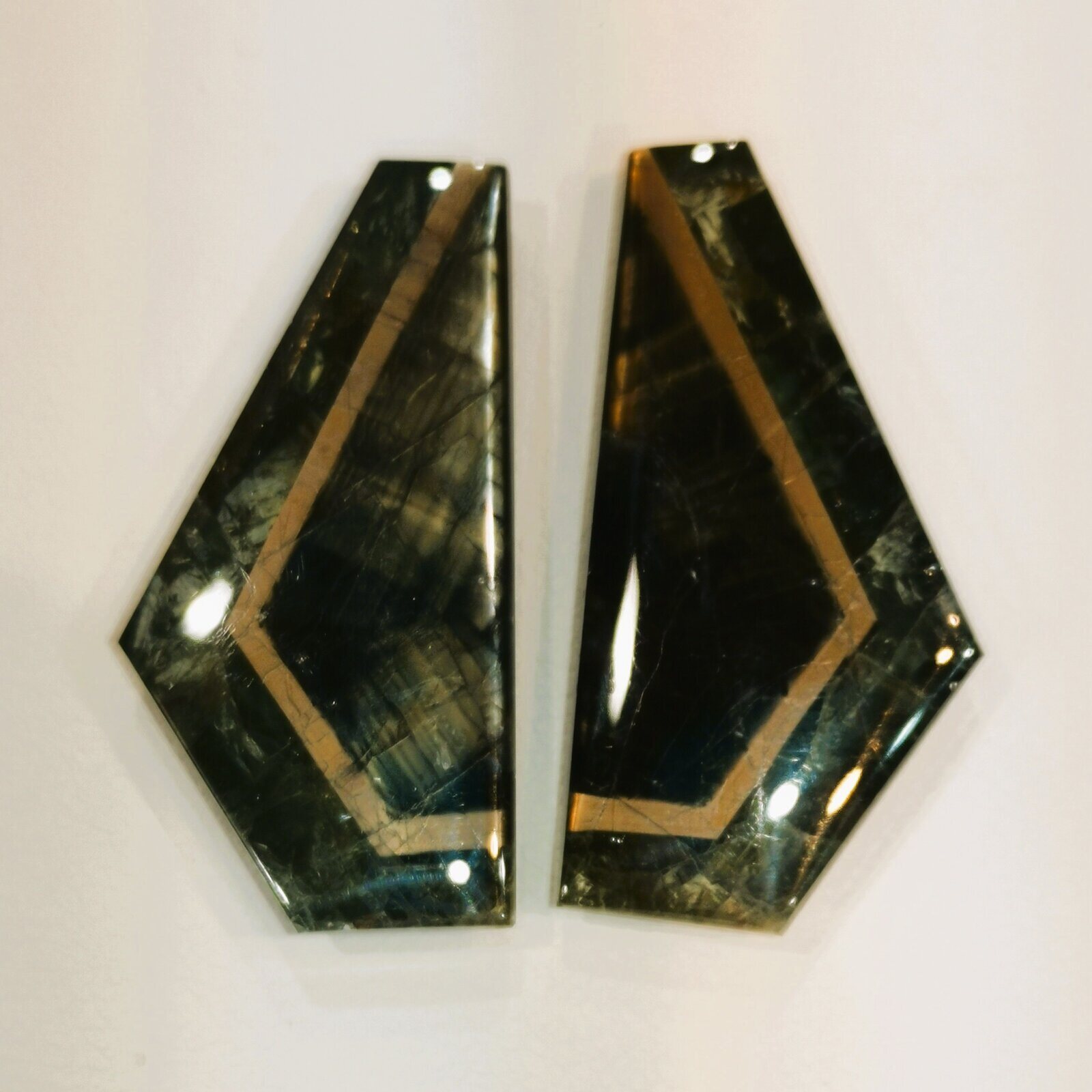 Two dark freeform gold sheen sapphire cabochons, each crossed by straight angular gold bands.