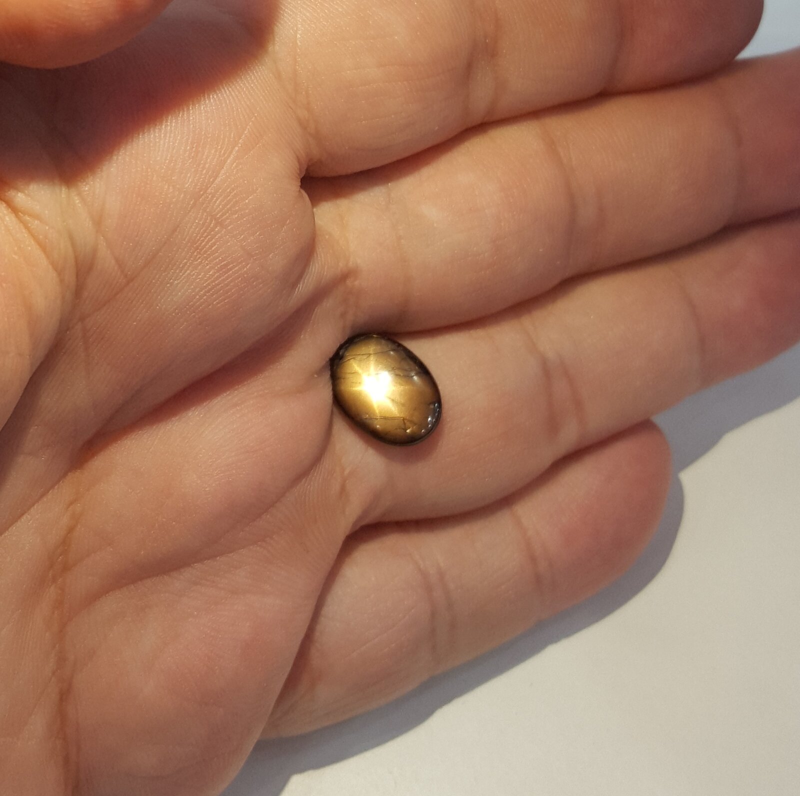 Small oval golden-brown cabochon on an open palm, showing a bright six-rayed star.