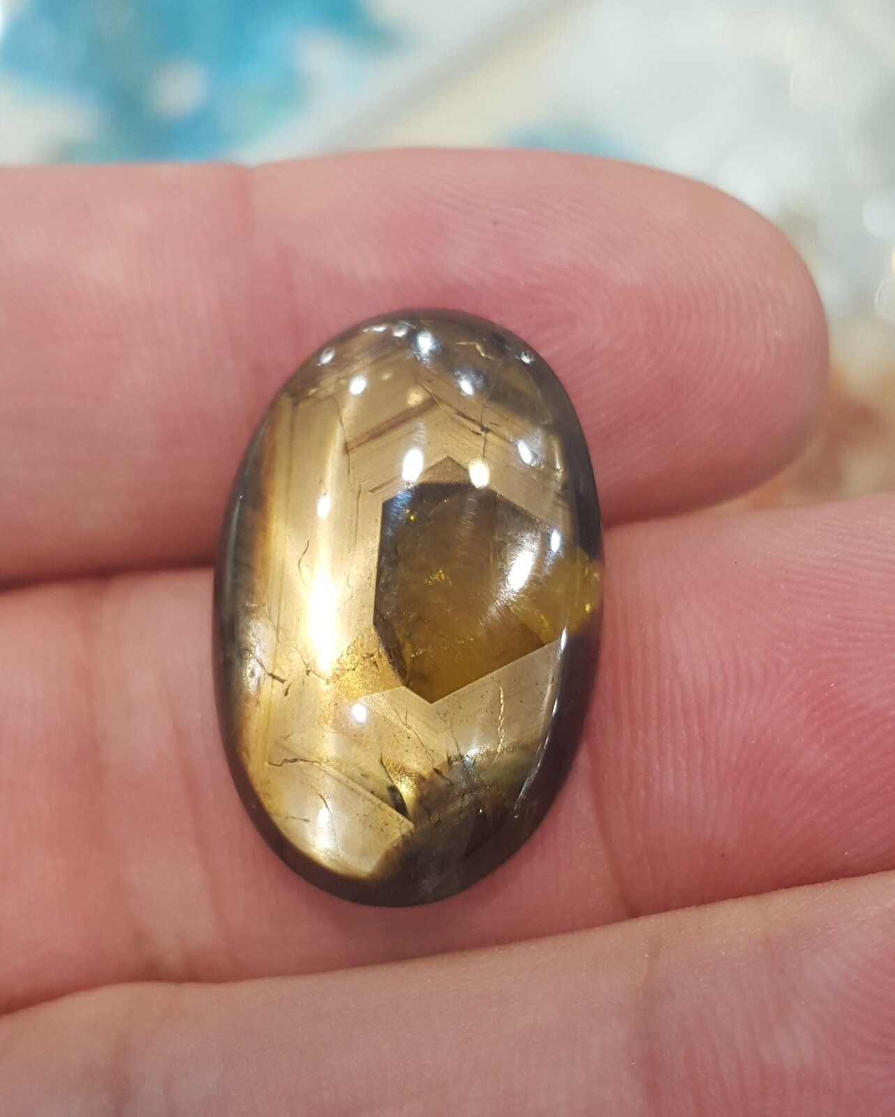 Oval brown gold sheen sapphire cabochon with a clearer centre, framed by angular golden bands meeting at hexagonal angles.